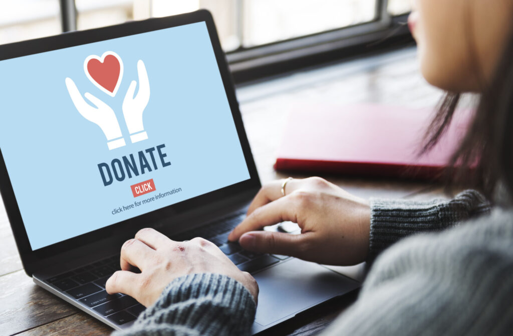 A person on a laptop donating online to a charity which is tax deductible in Canada.