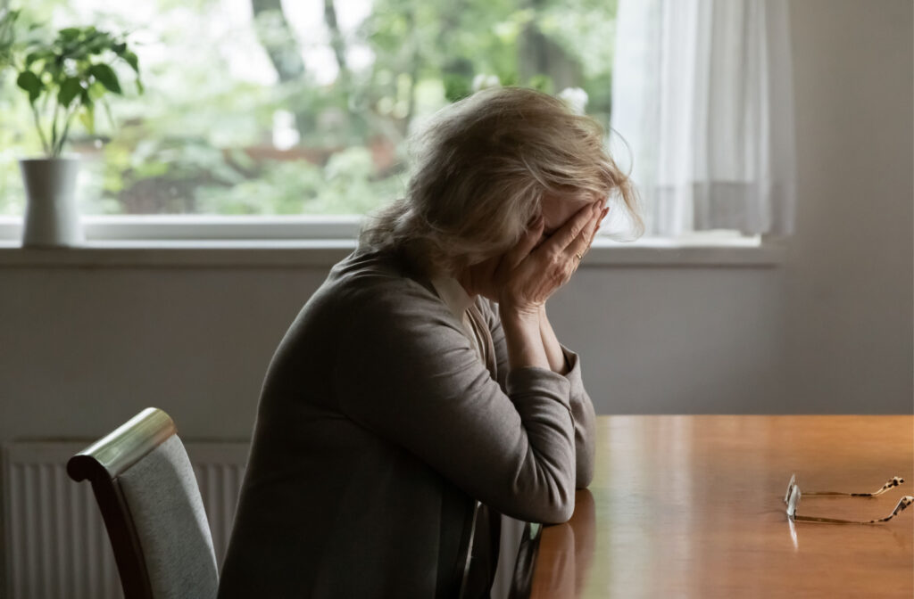 A woman sitting at a dining table with her head in her hands because she is experiencing grief.