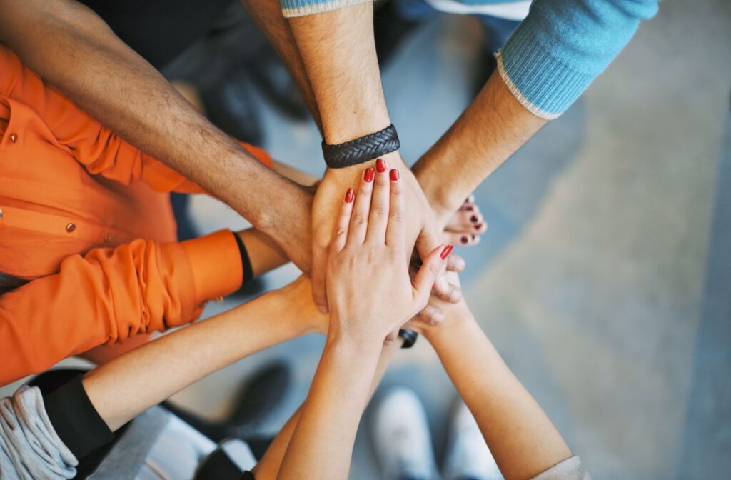 A bird's eye view of hands stacked in the middle of a circle to represent teamwork while volunteering.